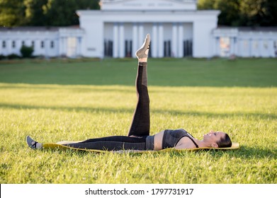 Beautiful young woman lying on a yellow mattress, pose while wearing a tight sports outfit in the park doing pilates or yoga, one leg circle intermediate exercises - Shutterstock ID 1797731917