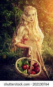 Beautiful young woman with magnificent blonde hair standing outdoor with a basket with apples. Countryside. 