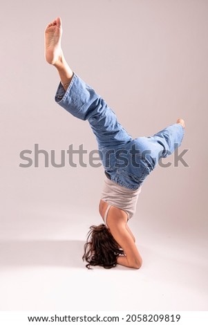 Beautiful young woman makes stand on her head with legs apart - an exercise of yoga. Female acrobat stand and balance on her hands and head whit her legs in the air. isolated 