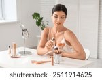 Beautiful young woman with makeup brushes and different cosmetic products at table in salon