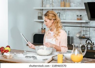 beautiful young woman making dough and using tablet at kitchen - Powered by Shutterstock