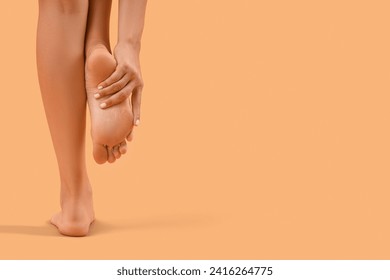 Beautiful young woman making foot massage on orange background, back view - Powered by Shutterstock