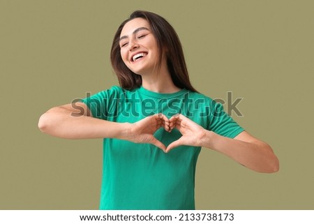 Beautiful young woman making heart with her hands on green background
