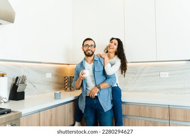 Beautiful young woman and man smiling making eye contact while hugging relaxing in their luxury white kitchen - Powered by Shutterstock