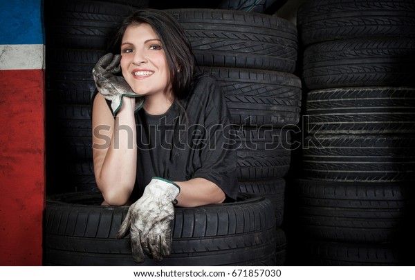 Beautiful young woman mechanic with helmet and\
protective gloves at work in auto service station. Concept works\
with tires on wheels