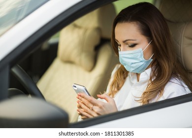 Beautiful Young Woman In A Medical Mask Driving A Car With A Mobile Phone