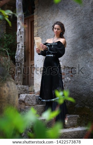 A beautiful young woman in a medieval dress reads a letter in front of an ancient castle
