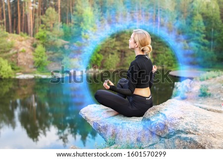 Beautiful young woman meditating near lake