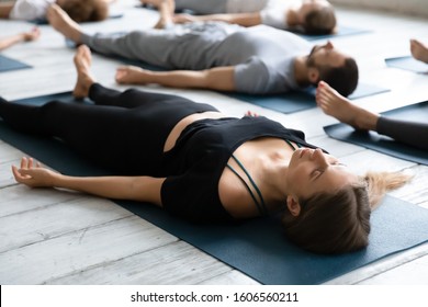 Beautiful young woman meditating in Savasana pose on floor close up, practicing yoga at group lesson, doing Corpse exercise on mats, training, working out in modern yoga studio, center - Powered by Shutterstock