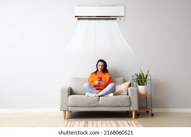 Beautiful Young Woman With Mobile Phone Resting On Sofa In Light Room With Operating Air Conditioner