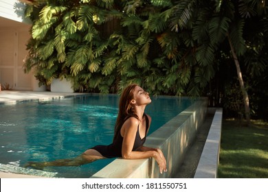 Beautiful young woman model in back bikini lies in swimming pool, posing and tanned on summer vacation. Healthy body care