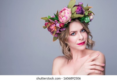 beautiful young woman model with bright flowers on her head on gray background