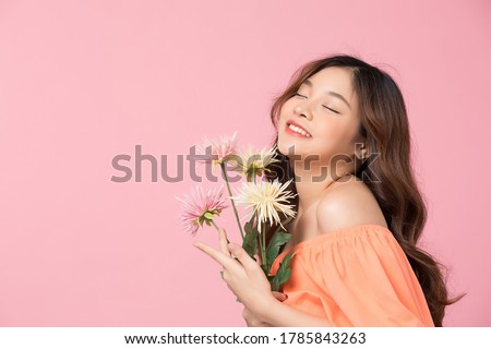 Beautiful young woman model with flowers posing isolated on pink studio background