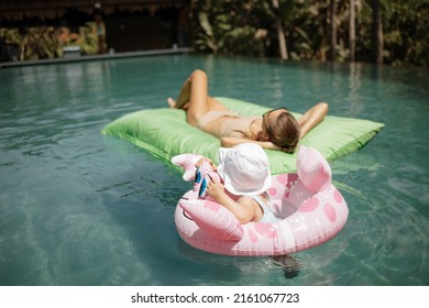 Beautiful Young Woman Mother In A Light Bathing Suit Lies In The Pool With A Child. Child In An Inflatable Circle. Happy Family On Vacation