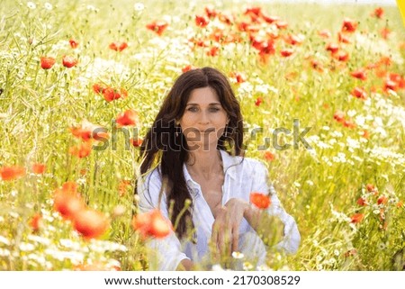 Beautiful young woman in national Ukrainian costume in a field with poppy flowers.