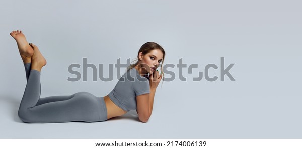 Beautiful young woman with natural make-up and\
gathered hair, dressed in a gray sports uniform, posing in the\
studio on a gray background.Advertising sportswear and yoga wear.\
Healthy lifestyle,\
sport