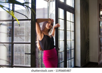 Beautiful young woman near a huge window. Attractive cute brunette in a stylish skirt. Opens a window, bright interior