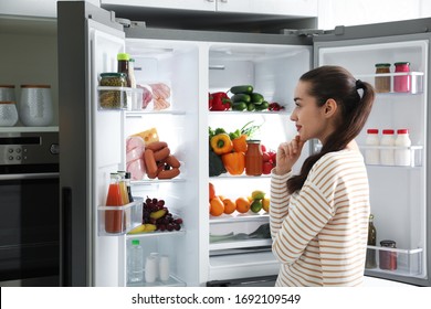 Beautiful Young Woman Near Open Refrigerator In Kitchen