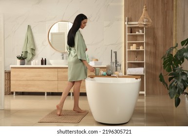 Beautiful young woman near tub in bathroom - Powered by Shutterstock