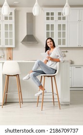 Beautiful young woman with notebook sitting on stool in kitchen