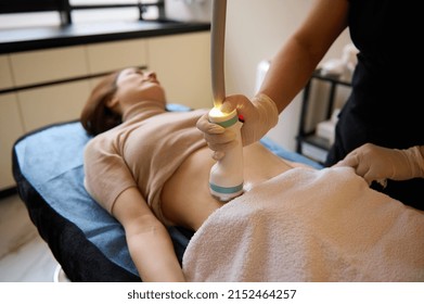 Beautiful young woman on a daybed receiving hardware spa procedure for cellulite reduction and weight loss in medical clinic.
