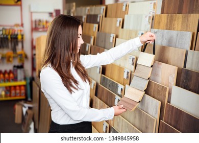 Beautiful young woman on position of manager or seller with dark hair looks at different types and colors of floor coloring in a small store
