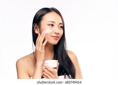 Beautiful Young Woman On White Isolated Background Applies Cosmetic Face Cream, Asian.