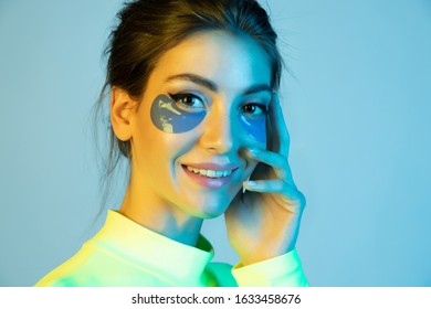 Beautiful young woman with patches for skin care around eyes. Cosmetic product for quickly moisturize, smooth out fine wrinkles, protection from bruises and dark circles. Studio portrait in neon light
