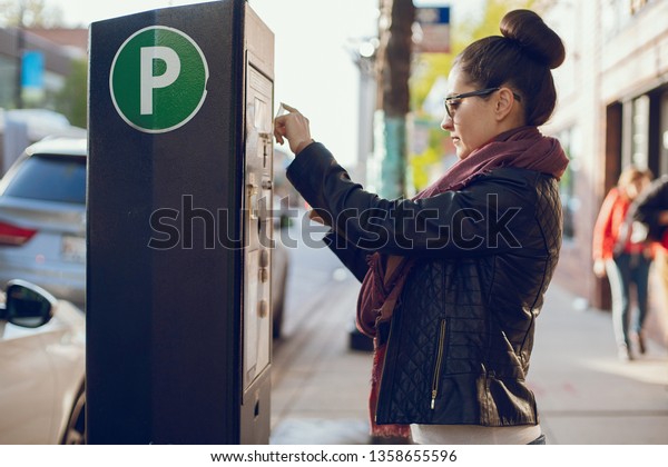 beautiful young woman pays for Parking in meter on\
the street
