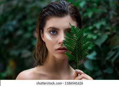 Beautiful young woman with perfect skin and natural make up posing front of plant tropical green leaves background with fern. Teen model with wet hair care of her face and body. SPA, wellness