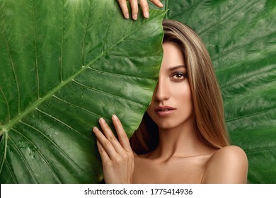 Beautiful Young Woman With Perfect Skin And Natural Make Up Posing Front Of Plant Tropical Green Leaves Background With Fern. Teen Model With Wet Hair Care Of Her Face And Body. SPA, Wellness