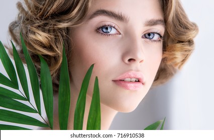 Beautiful young woman with perfect skin and natural make up. Teen model with green leaves. SPA,  skincare and wellness. Close up, selective focus.