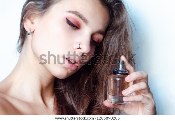 \
Beautiful young woman with pierced nose\
ring and bright make-up with perfume bottle at\
home