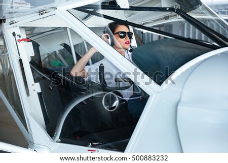 Beautiful young woman pilot in sunglasses and headset sitting in cabin of small aircraft