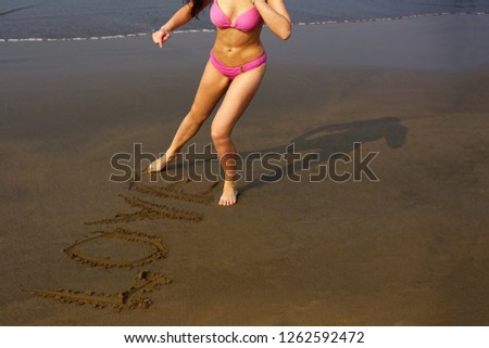        A beautiful young woman in pink bikini writing a Love sign on the beach near the ocean                        