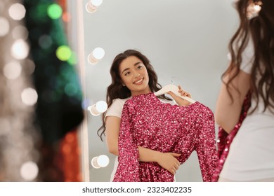 Beautiful young woman with pink sequin dress near mirror in boutique. Choosing party clothes - Powered by Shutterstock