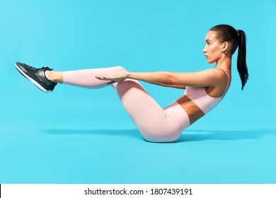 Beautiful young woman in pink sportswear doing fitness exercise sit-ups, abs. On blue background