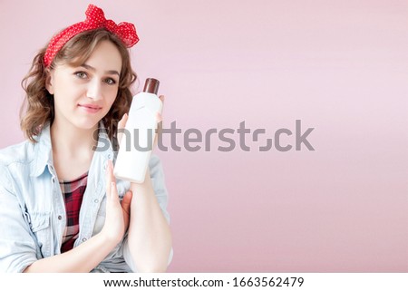 Beautiful young woman with pin-up make-up and hairstyle with cleaning tools on pink background.