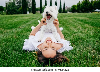 Beautiful young woman playing with her little west highland white terrier in a park outdoors. Lifestyle portrait. - Powered by Shutterstock