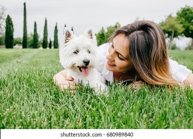 Beautiful young woman playing with her little west highland white terrier in a park outdoors. Lifestyle portrait. - Powered by Shutterstock