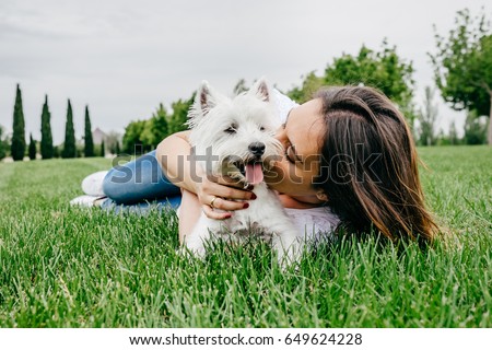 Beautiful young woman playing with her little west highland white terrier in a park outdoors. Lifestyle portrait.