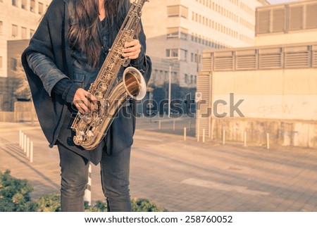 Beautiful young woman playing tenor saxophone in the city streets