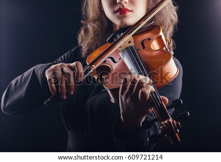 Beautiful young woman playing the violin on dark background