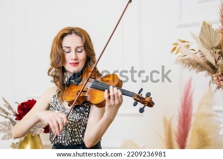 beautiful young woman plays the violin surrounded by flowers on light background