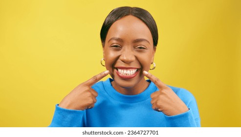 Beautiful young woman points to smile, white teeth, happy in yellow studio - Shutterstock ID 2364727701