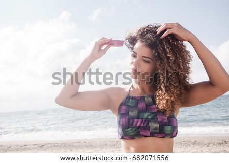 Beautiful young woman portrait combing her curly hair on the beach