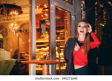 Beautiful Young Woman Poses Near Bright Cafe On The Street At Night