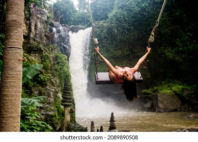 Beautiful young woman posing at the great Tegenungan waterfall in the deep rainforest of Bali island, Indonesia.