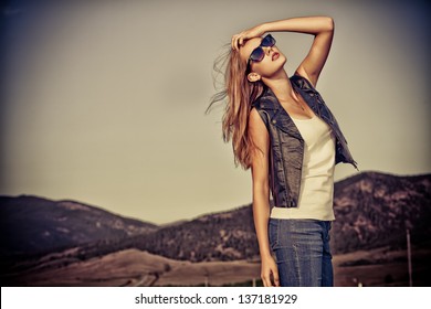 Beautiful young woman posing on a road over picturesque landscape.