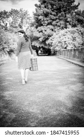 Beautiful young woman posing in vintage 1940s clothes, walking away with a suitcase